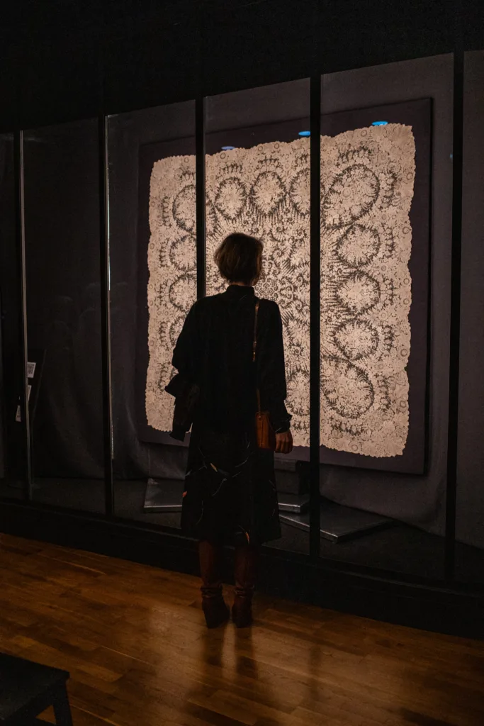 Grande dentelle blanche de plus ou moins 2 mètre sur 2 avec une visiteuse l'admirant